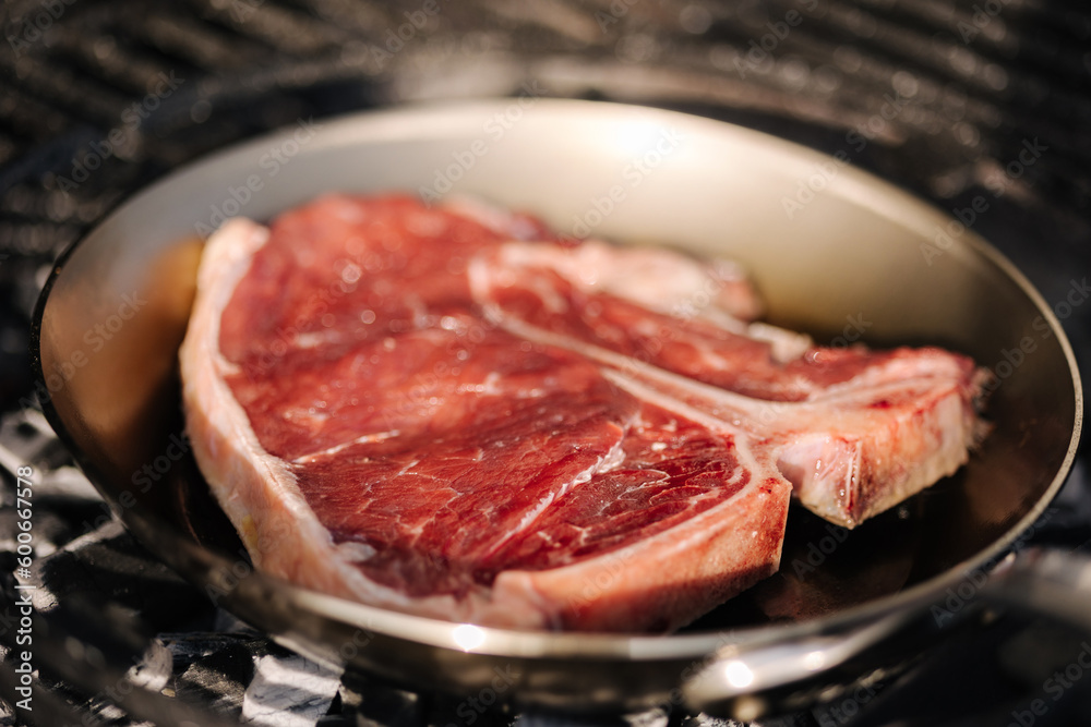 Tasty beef T-bone steak is fried in a carbon steel pan that stands on hot coals. BBQ concept. Close-up