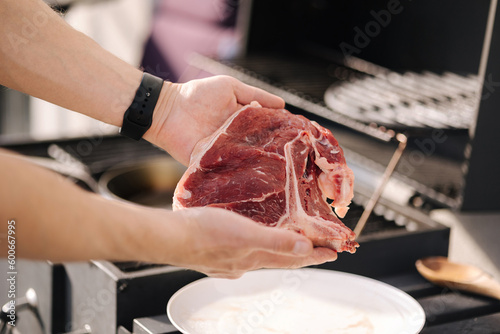 Human hand hold T-bone Steak in front of grill. BBQ concept. Close-up