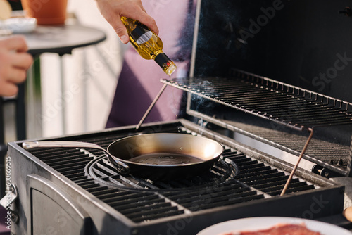 Close-up of man add olive oil on frying carbon steel pan which is on the grill. 