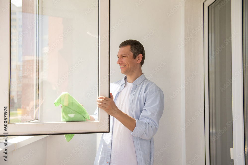 Fototapeta premium Happy man is cleaning the house. Wash windows with a rag on the balcony