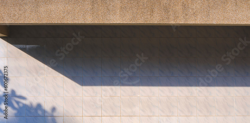 Sunlight and shadow of exposed aggregate finish cobblestone awning on surface white tile wall background in panoramic view 