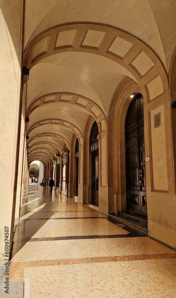 Portico in bright yellow or orange (light) colors in Bologna, Italy, with marble floor and arched stone walls - metal bars in front of window for safety