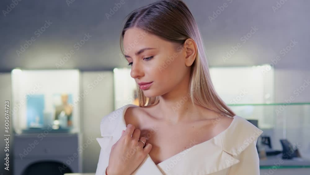 Pretty graceful girl with a beautiful face and a diamond gold ring posing in a jewelry store with accessories. Positive blonde girl in a white jacket is trying on a wedding ring. Jewelry advertising. Pretty graceful girl with a beautiful face and a diamond gold ring posing in a jewelry store with accessories. Positive blonde girl in a white jacket is trying on a wedding ring. Jewelry advertising.