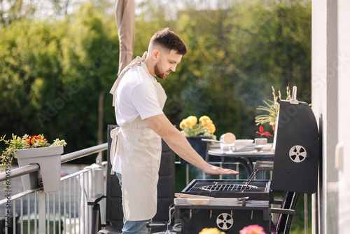 Foto Side view of handsome man try how hot is BBQ grill