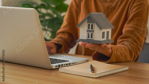 Female woman hands holding home model, small miniature white toy house. Mortgage property insurance dream moving home and real estate concept.