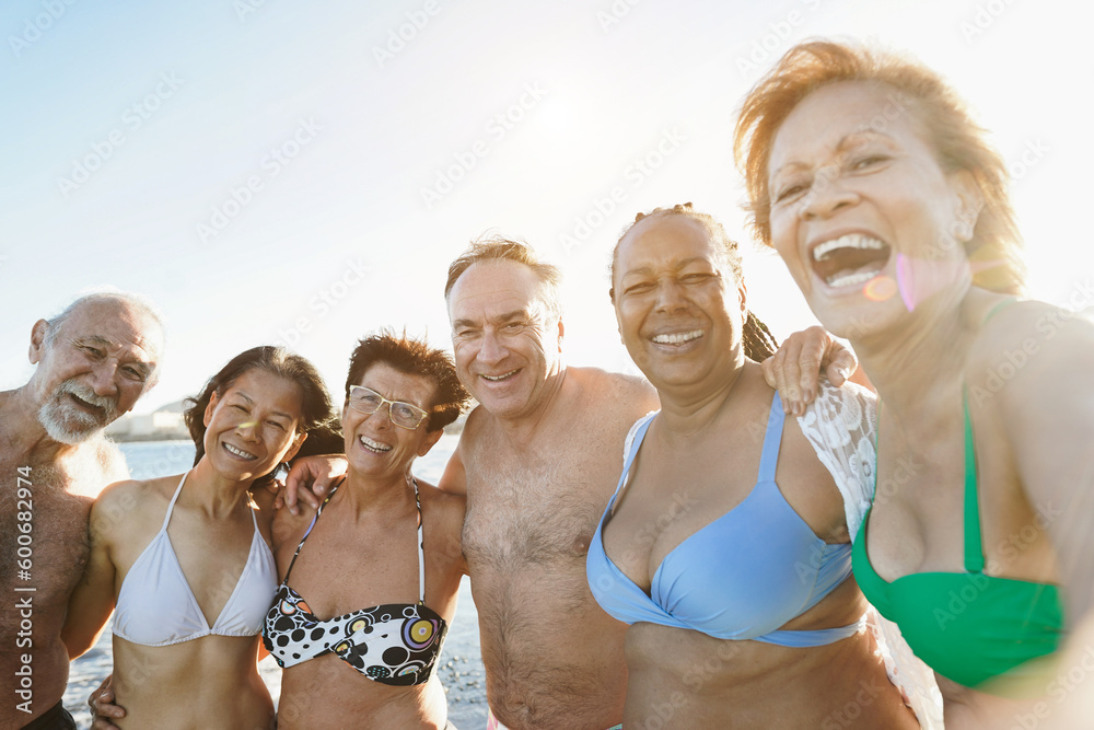 Multiracial senior people taking selfie on the beach during summer vacation - Joyful elderly lifestyle concept, travel and multiracial concept - main focus on center man face
