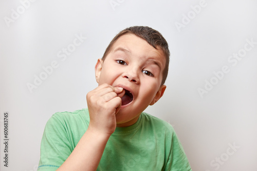 A handsome boy of 6-7 years tries to shake a baby tooth with his finger.