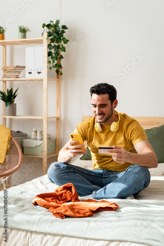 Man sitting on bed doing online shopping with smart phone.