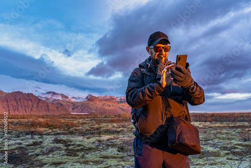 Obraz na płótnie man holds a glove with teeth and using a phone for navigation with mountains with snow on background during sunset in iceland w salonie