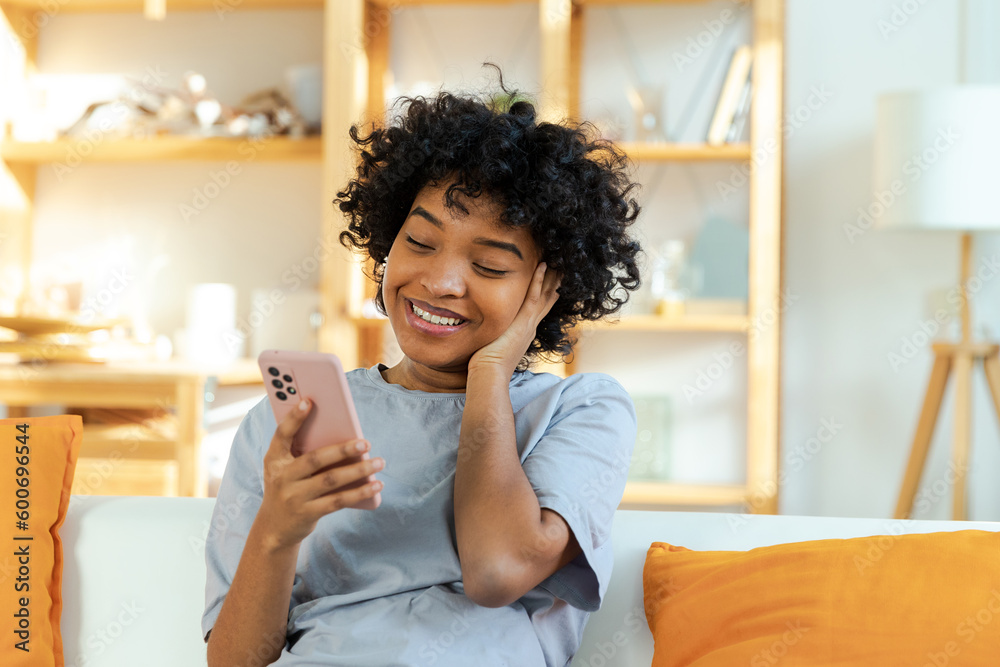 Excited happy young black african american woman holding cell phone laughing feeling joy getting mobile message. Overjoyed girl laughing aloud sitting on couch watching funny video reading news Excited happy young black african american woman holding cell phone laughing feeling joy getting mobile message. Overjoyed girl laughing aloud sitting on couch watching funny video reading news