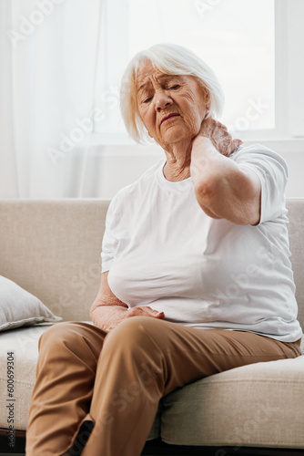 Elderly woman severe neck pain sitting on the sofa, health problems in old age, poor quality of life. © SHOTPRIME STUDIO