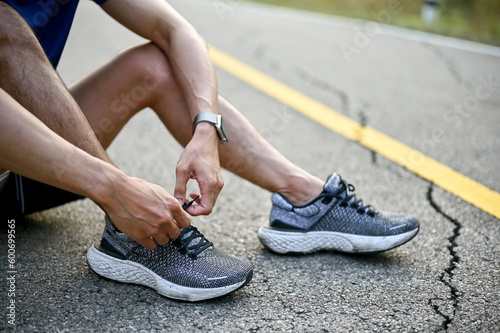 A man sits on street and tying his sport shoes laces, preparing for running