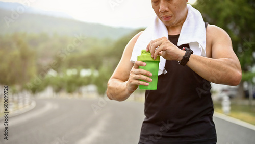 Fotografía Cropped image, Sweaty and thirsty mature Asian man drinks water