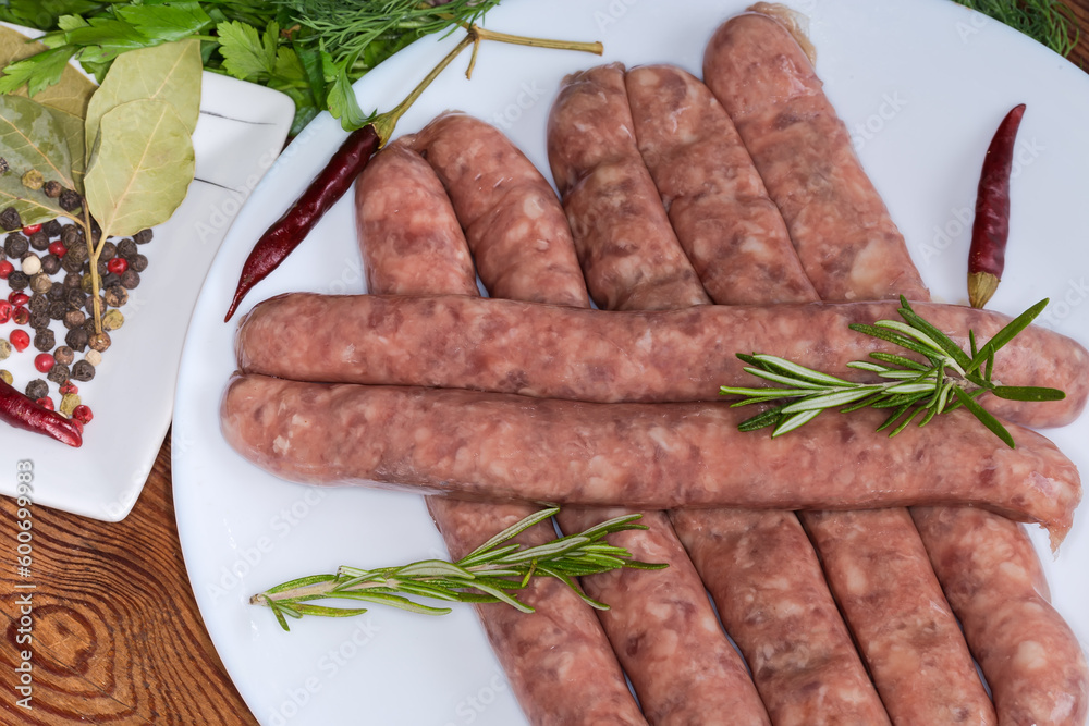 Raw sausages among spices and greens on dish close-up Raw sausages among spices and greens on dish close-up