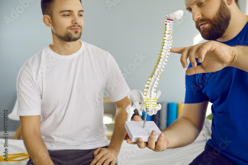 Young man with spine problems on consultation with osteopath showing him backbone layout in clinic. Chiropractor talking about backbone problems. Checkup, prevention examination, diagnosis concept.