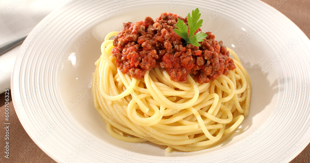 spaghetti bolognese on a white plate. classic italian pasta with meat tomato sauce on a brown background. dish of mediterranean cuisine. food on the table on a sunny day. yellow noodles, minced meat.