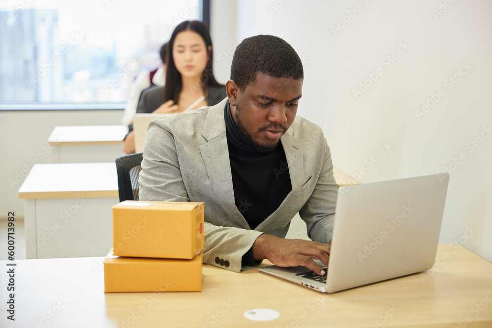 African businessman using laptop computer and checking parcel cardboard boxes from online shopping in the office African businessman using laptop computer and checking parcel cardboard boxes from online shopping in the office