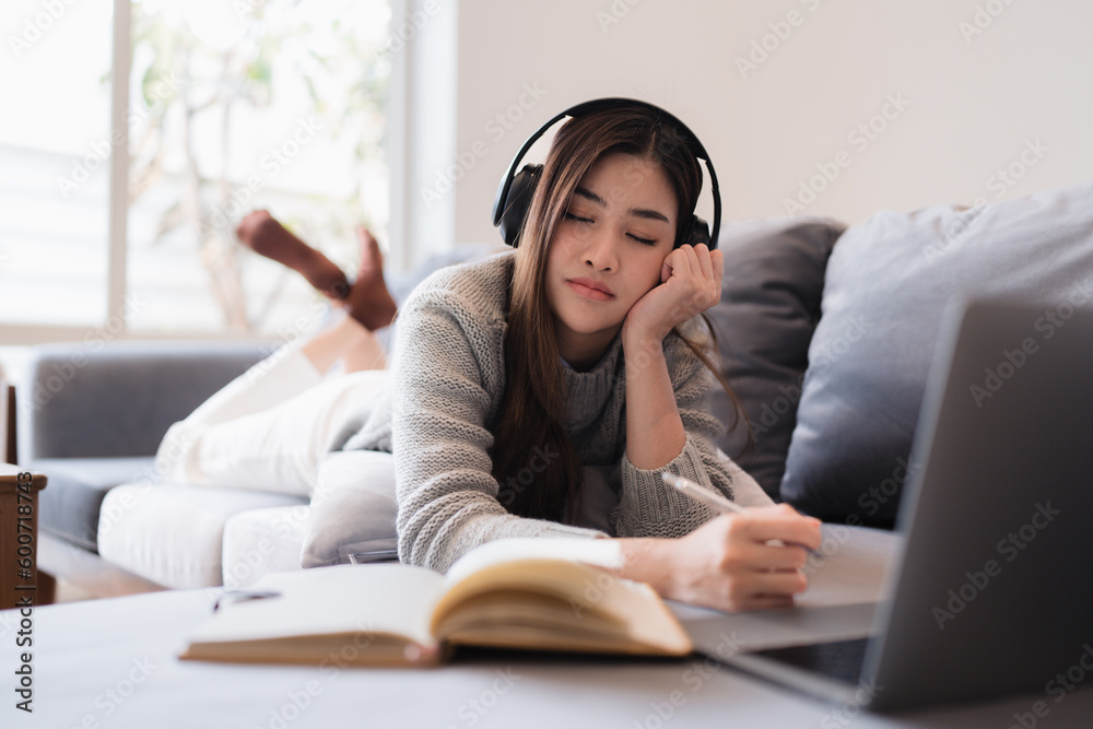 Online education, e-learning. Asian woman in stylish casual clothes, studying using a laptop, listening to online lecture, taking notes, online study at home Online education, e-learning. Asian woman in stylish casual clothes, studying using a laptop, listening to online lecture, taking notes, online study at home