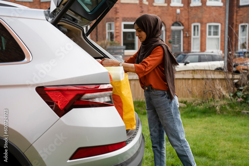Photography Woman wearing hijab unloading shopping bags from car trunk