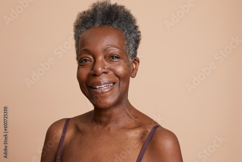 Portrait of smiling senior woman against beige background