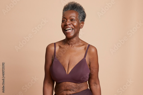 Studio shot of senior woman in underwear laughing against beige background