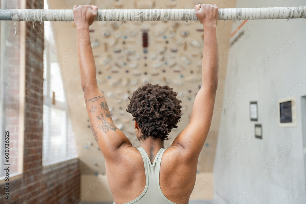 Fototapeta premium Woman performing chin-up exercise next to climbing wall