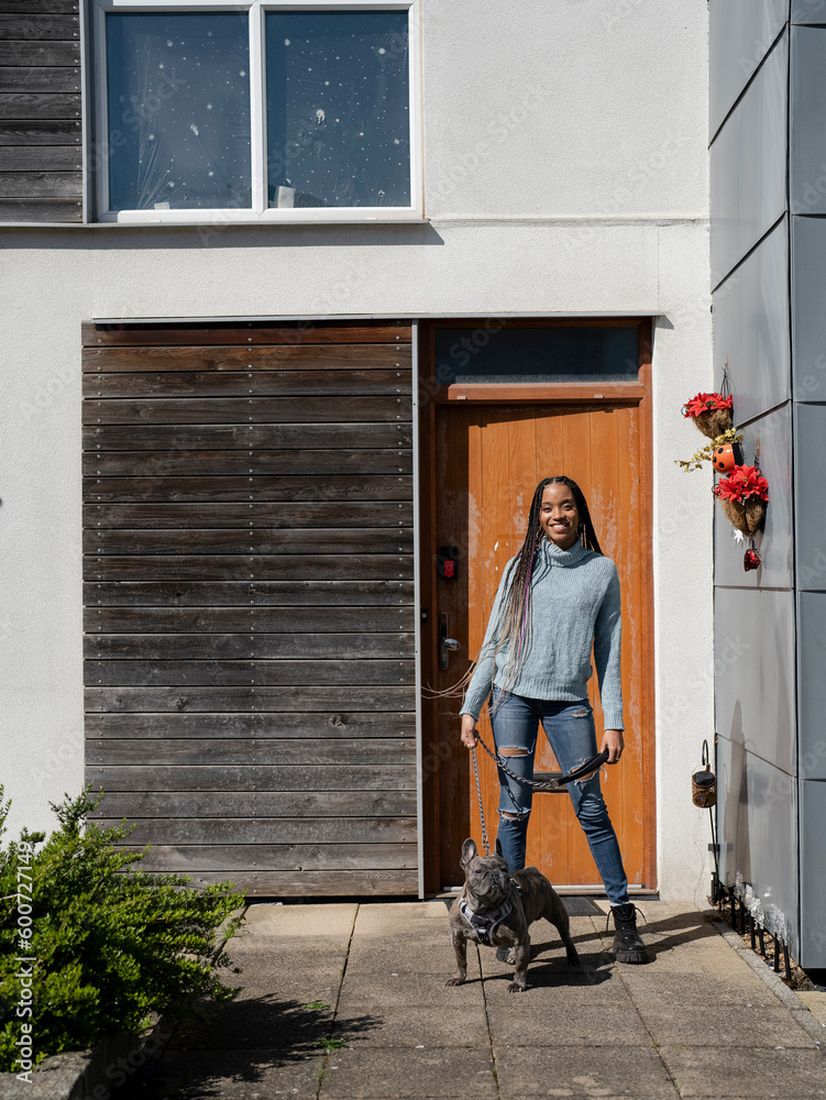 Smiling woman posing with dog in front of house on sunny day