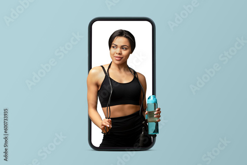 Smiling young black muscular woman athlete in sportswear and skipping rope hold bottle of water