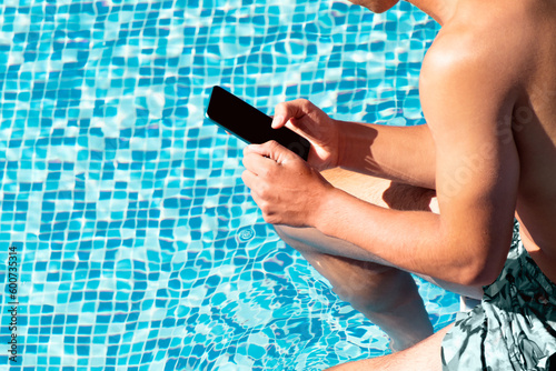 Obraz na plátně Young man using smartphone in resort hotel poolside during summer holidays, vacation