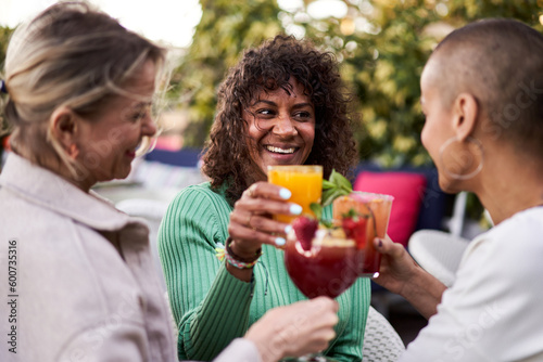 Three cheerful mature women having drinks outdoors in a terrace, toasting with cocktails or mocktails. Female friends having fun together gathering in a bar.