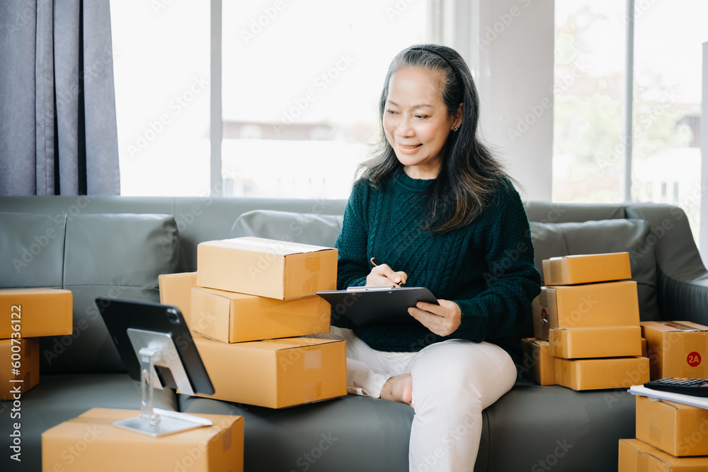 Startup small business SME, Mature woman hand using smartphone or tablet taking receive and checking online purchase shopping order to preparing pack product box. business online shopping concept Startup small business SME, Mature woman hand using smartphone or tablet taking receive and checking online purchase shopping order to preparing pack product box. business online shopping concept