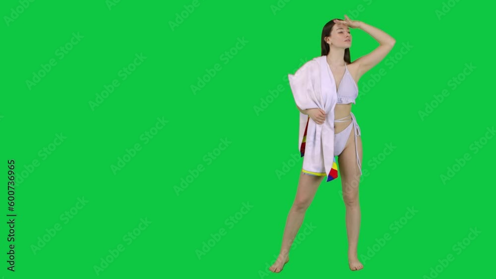 Model in a bikini and a towel looking of a spot and walking away in front of a green screen Model in a bikini and a towel looking of a spot and walking away in front of a green screen