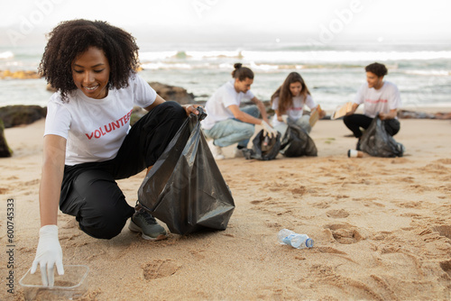 Positive young multiracial people volunteers in rubber gloves and african american lady with trash bag clean up