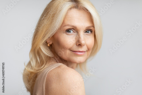 Portrait of happy senior woman with flawless skin and natural makeup posing on light background, free space
