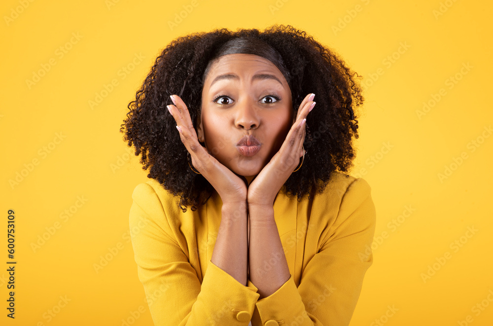 Portrait of black lady blowing kiss to camera and touching cheeks, posing on yellow studio background Portrait of black lady blowing kiss to camera and touching cheeks, posing on yellow studio background