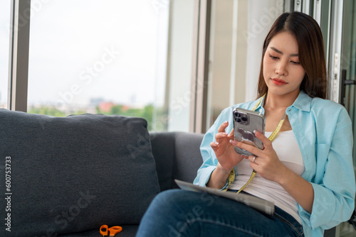 Young woman in casual wear, sits on a sofa, using smart phone, chatting in social media
