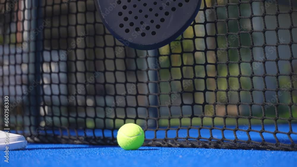 Closeup of a padel player picking up the racket and the ball by the net of the court and starting playing.