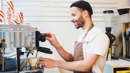 Happy male barista preparing coffee at espresso machine in cafe