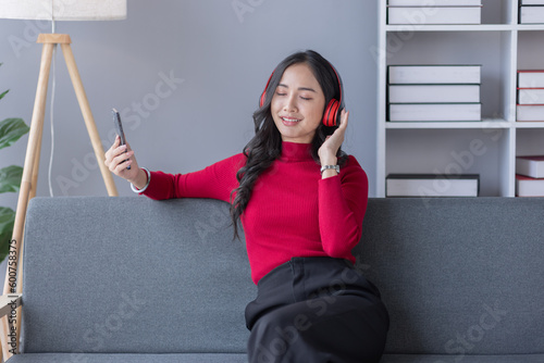 Beautiful Young asian woman at home sitting on the sofa while using laptop phone and headphone listening to music at home © David