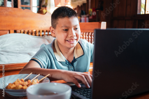 Asian man using laptop on wooden table with junk food at home in front of the window