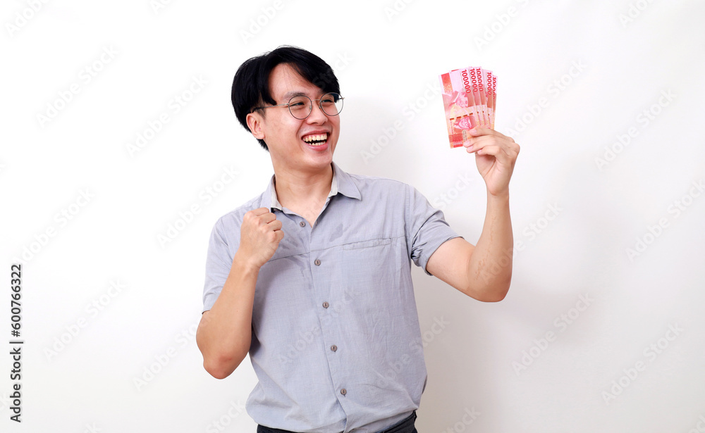 Happy asian man holding Indonesian banknotes while showing clenching hand Happy asian man holding Indonesian banknotes while showing clenching hand