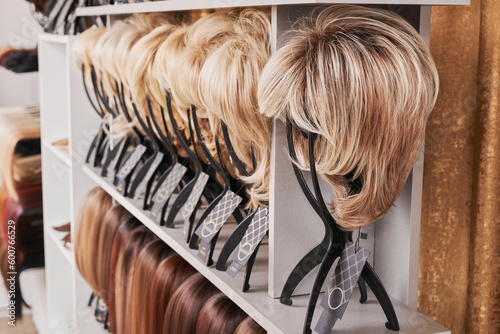 Showcase of natural looking wigs in different colors fixed on the metal wig holders in beauty salon. Row of mannequin heads with variation shades hair on shelf in wig shop.