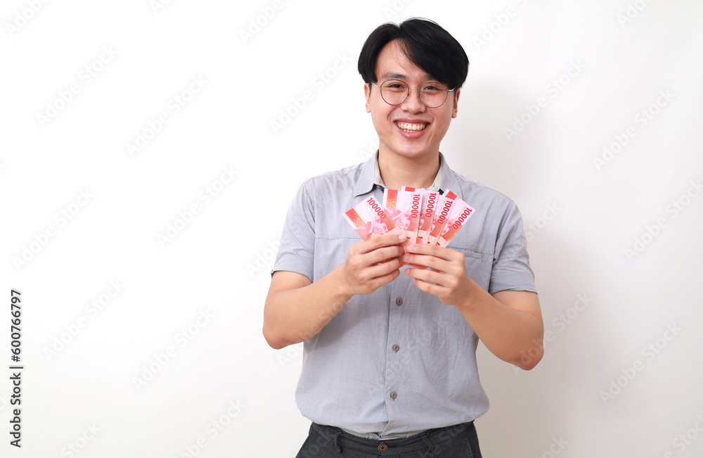 Happy asian man standing while holding Indonesian banknotes. Isolated on white Happy asian man standing while holding Indonesian banknotes. Isolated on white