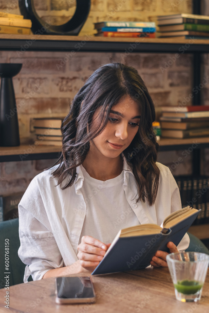 A young attractive dark-haired woman is reading a book in a cafe. A young attractive dark-haired woman is reading a book in a cafe.