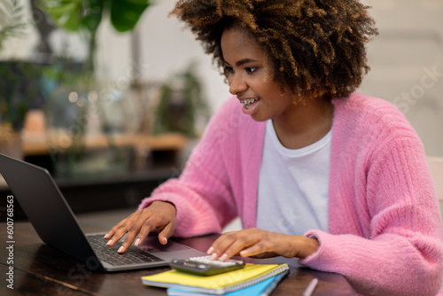 Happy black woman freelancer working from home, using laptop, calculator