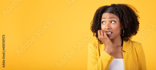Scared terrifying black lady with bushy hair gesturing and grimacing, looking aside at free space on yellow background
