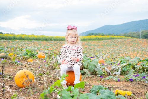 Cute Caucasian toddler girl sitting on a pumpkin at the farm during a pumpkin patch © Ana
