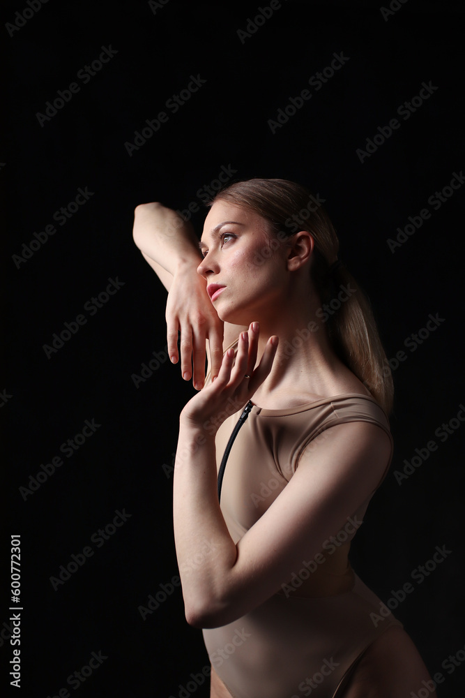 Ballerina in a beige bodysuit. Dark background. Sculpted beautiful female body. Pose of a gymnast. Ballerina in a beige bodysuit. Dark background. Sculpted beautiful female body. Pose of a gymnast.