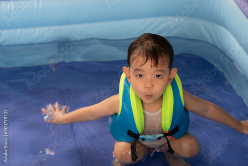 Happy Funny Baby Boy Kid Toddler wearing life jacket playing water in the pool