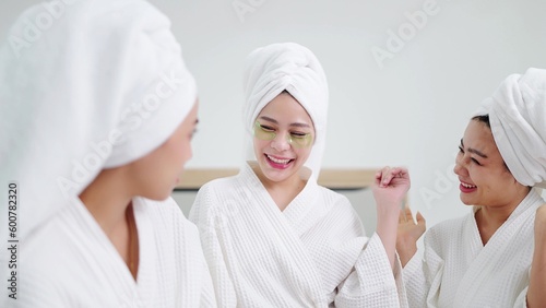 Group of beautiful young asian women in bathrobe and towels on heads with collagen patch on under eyes and enjoy talking together. Woman with under eye collagen pads